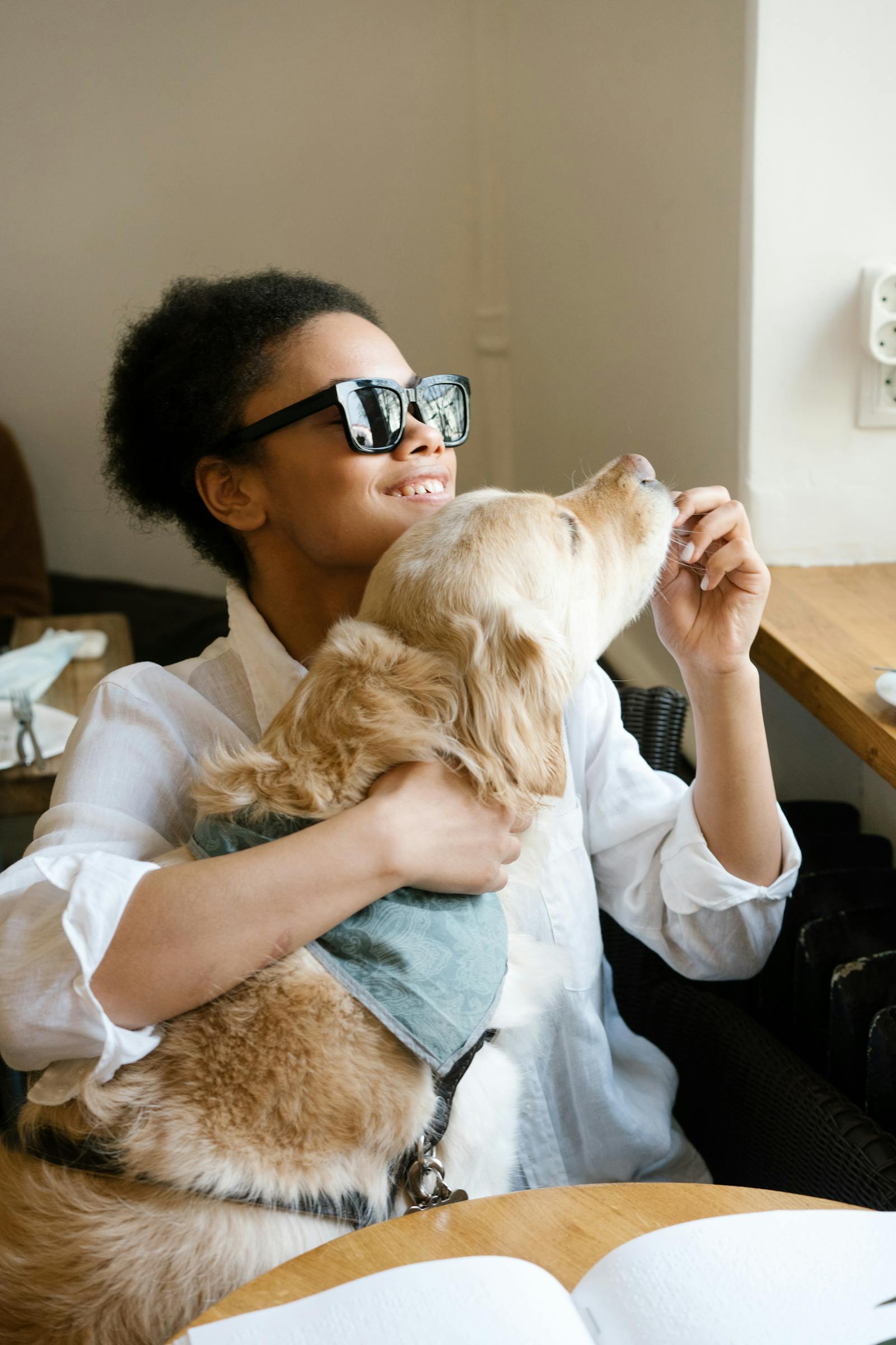 An adult woman in her 40s smiling with her assistance dog while seated at a table, reflecting confidence and independent living