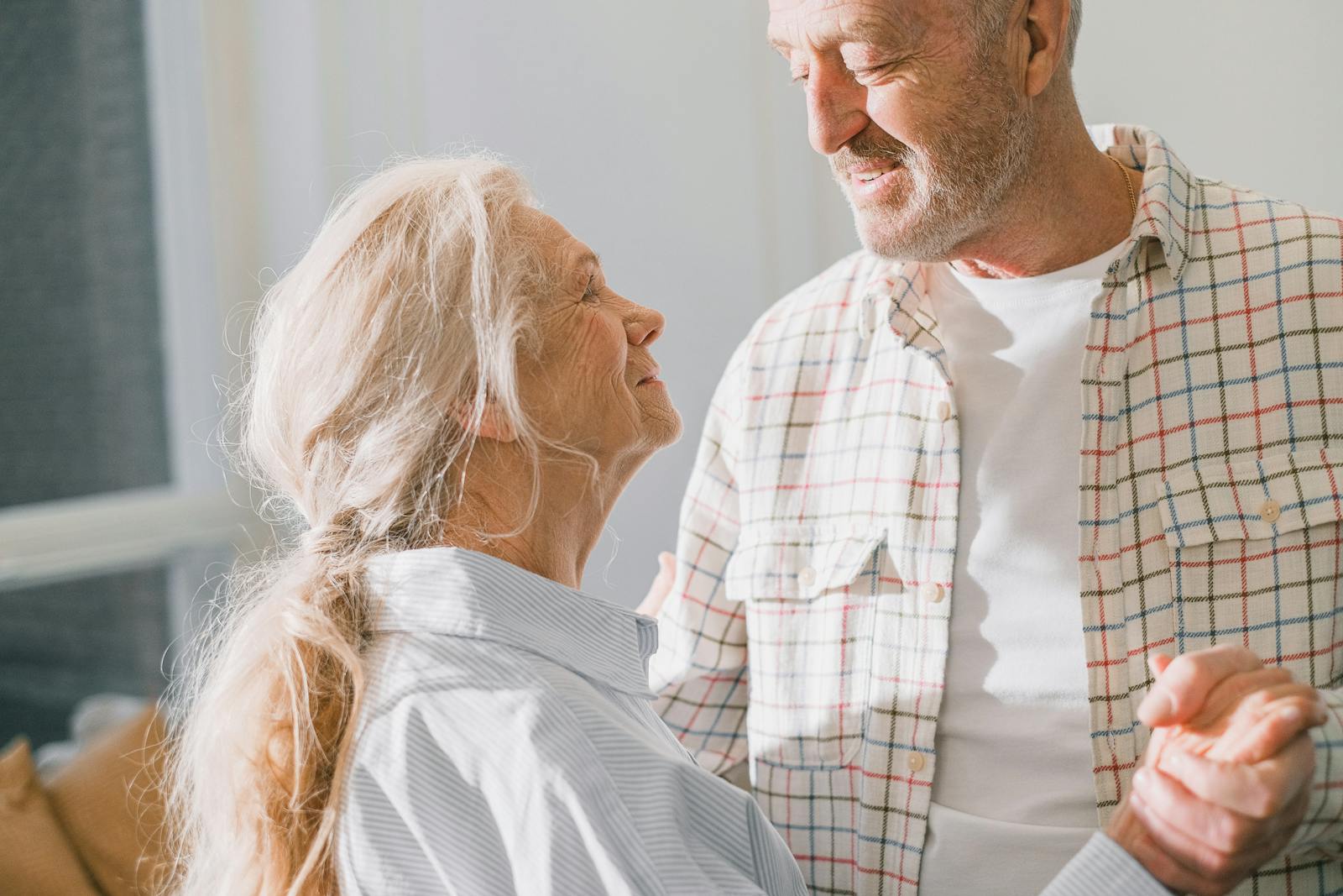 Two adults in their 20s to 40s smiling together at home in a warm, joyful moment
