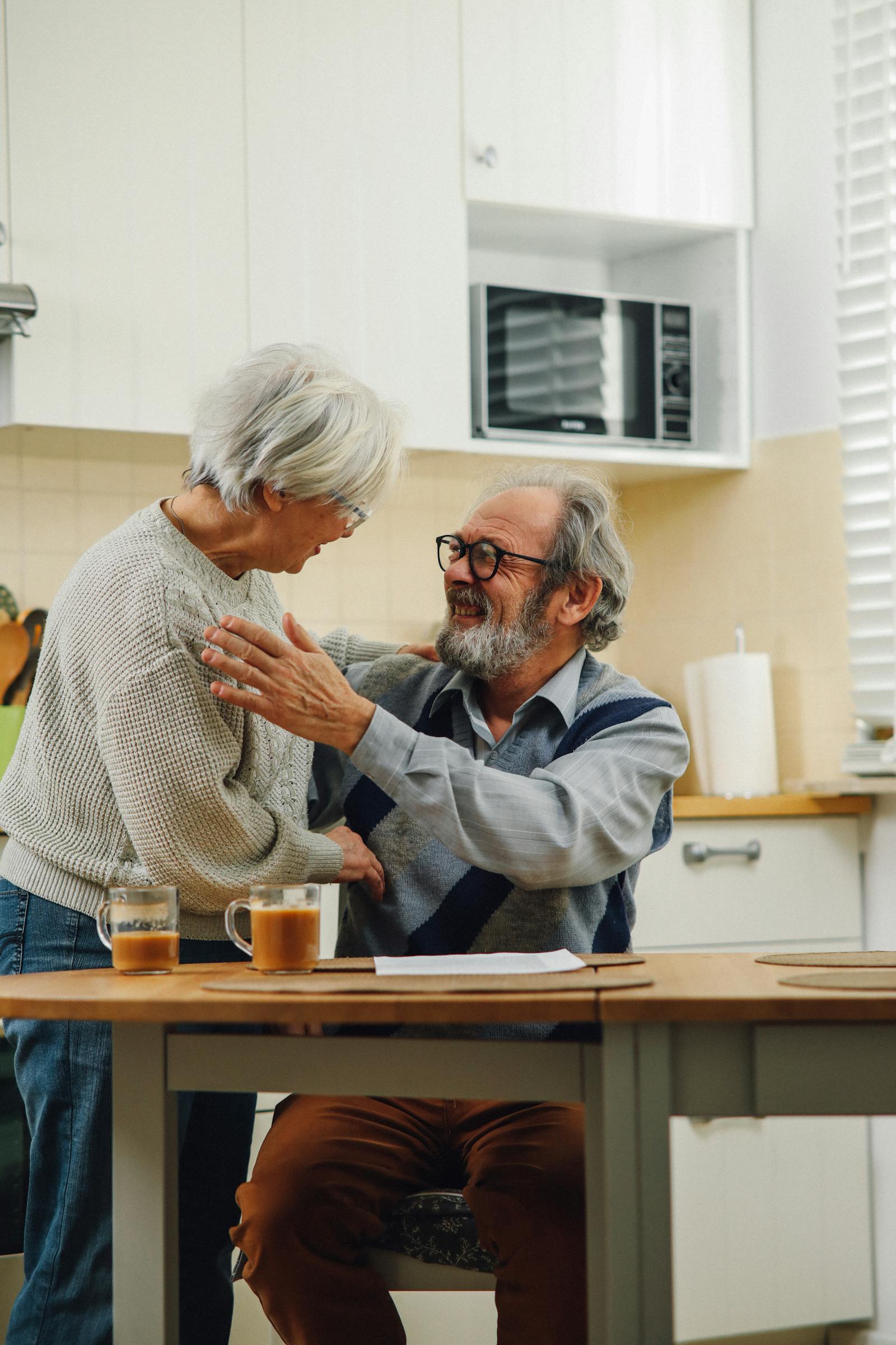 Two adults in their 30s smiling together in a bright kitchen at home