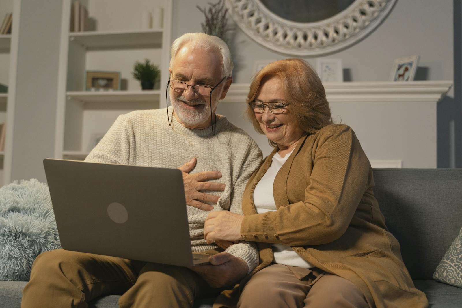 Two adults in their 30s to 50s smiling together while using a laptop at home